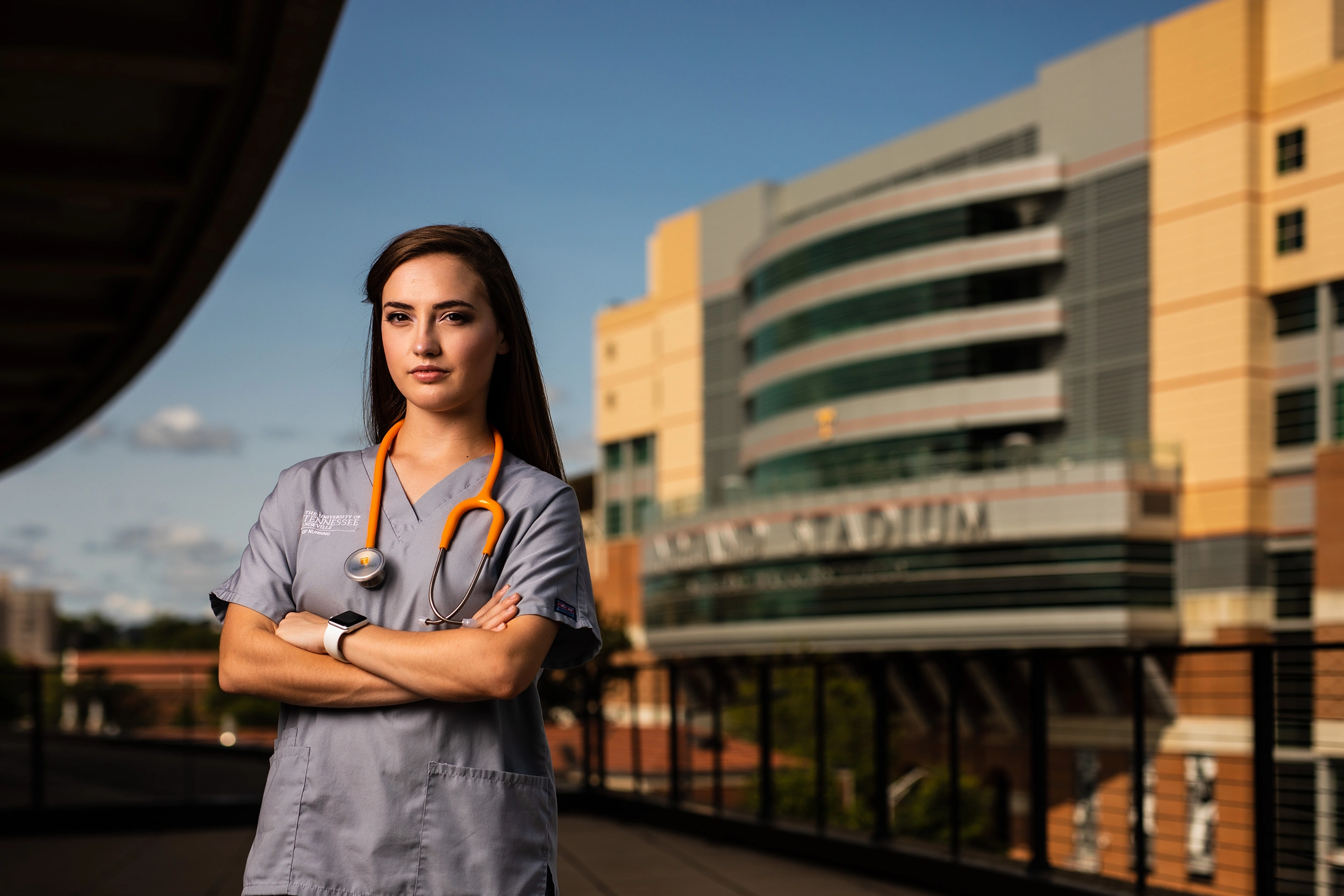A woman in scrubs with a stethoscope around her neck posing in front of Neyland Stadium for a photo