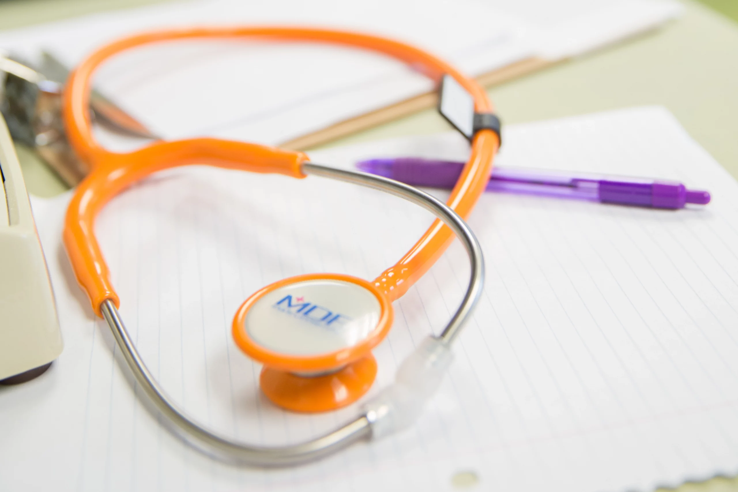 An orange stethoscope lying on sheets of paper