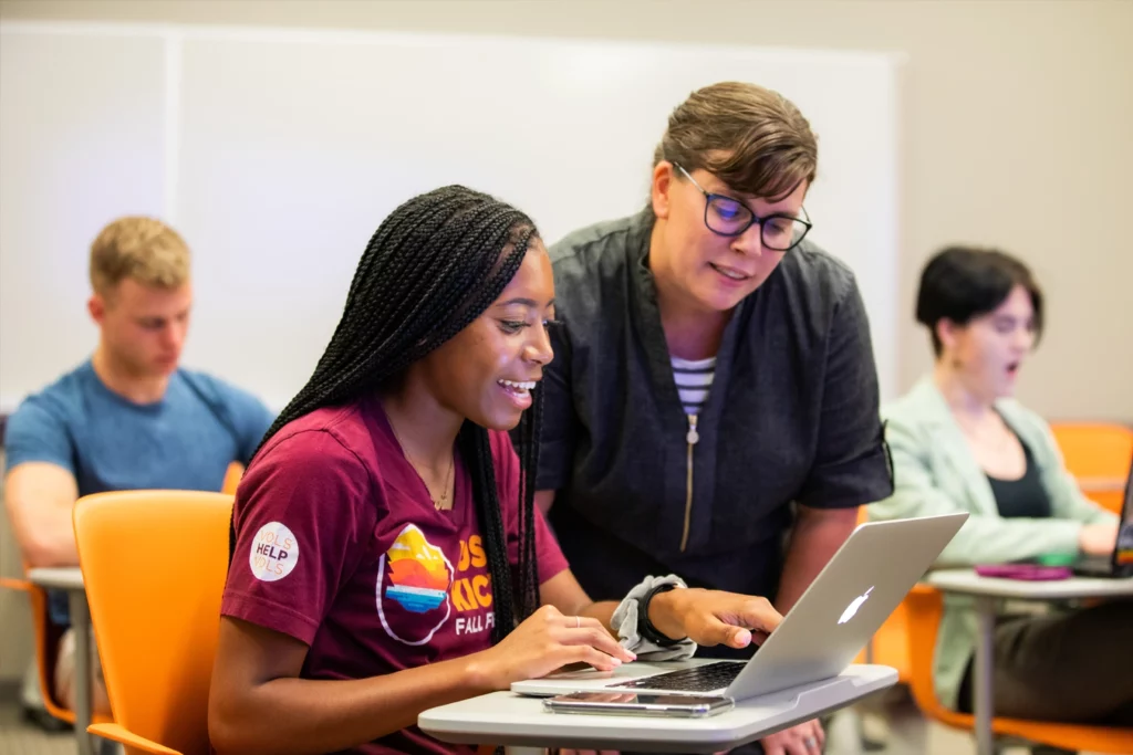A member of advising helps a student as she works on her laptop.