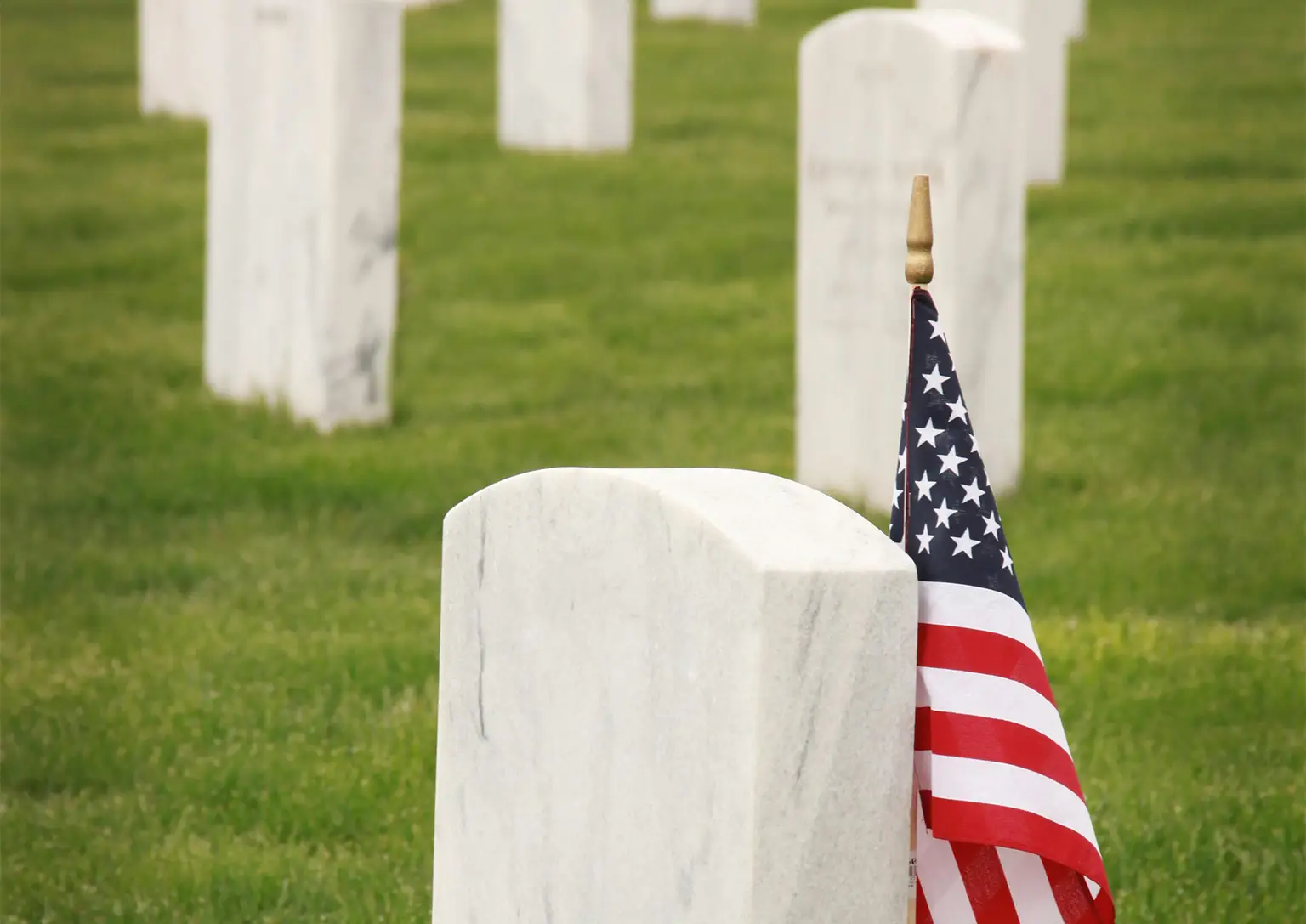 An American flag planted next to a headstone in a graveyard