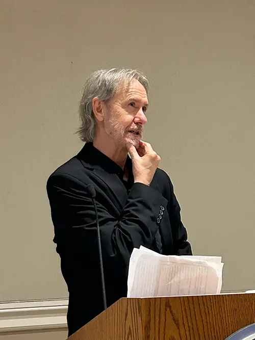 A male speaker strokes his chin during a talk at a lecturn