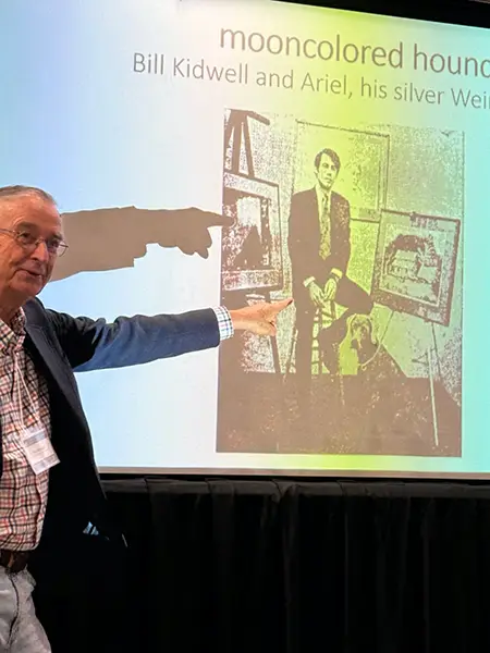 A male speaker points at an old photo as part of his powerpoint presentation