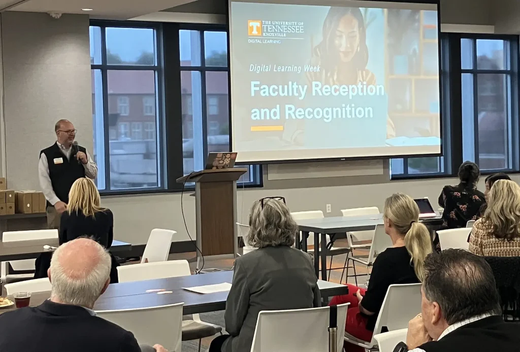 A speaker presents to a group around tables at the faculty recognition event