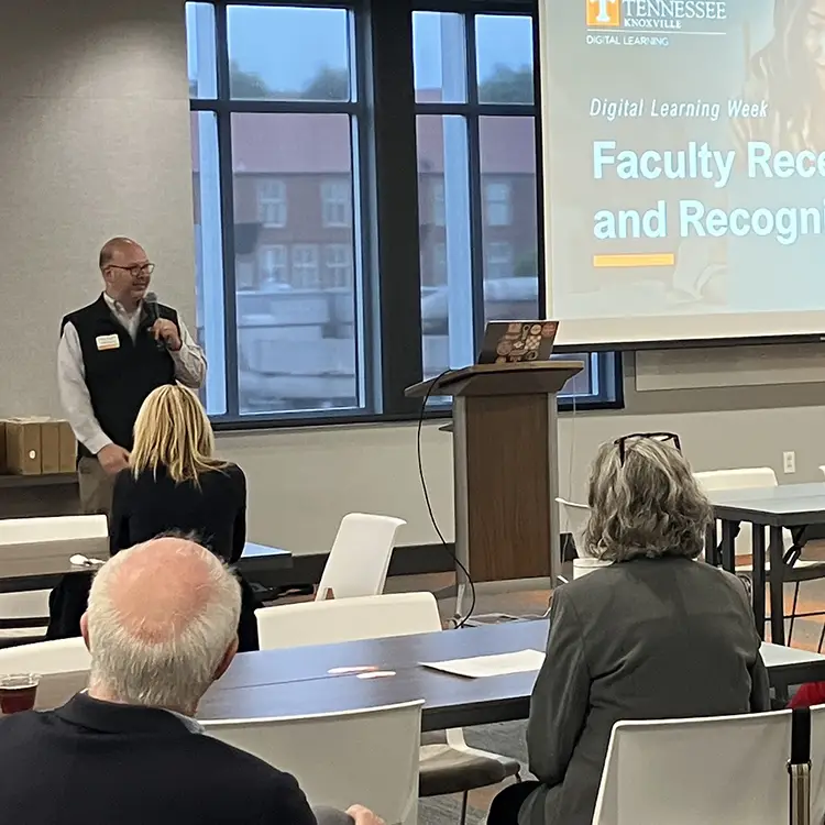 A speaker presents to a group around tables at the faculty recognition event