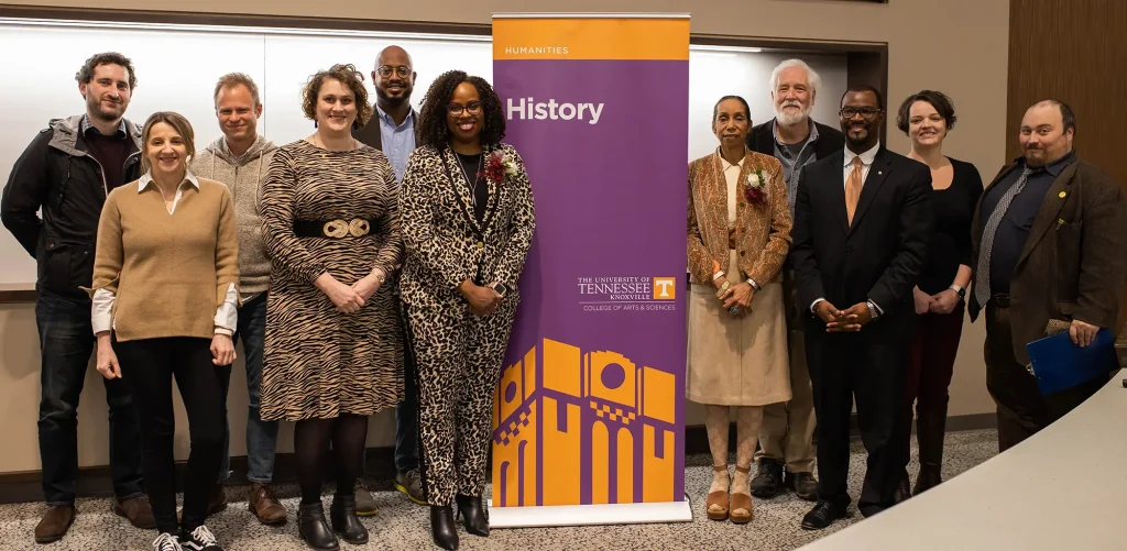 A group of people posing for a photo around a stand-up banner for the UT Department of History