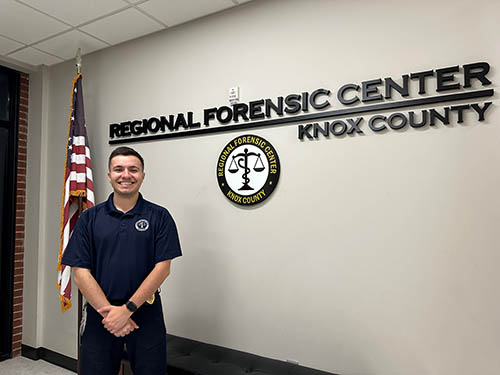 A man standing in front of a wall with the text Regional Forensic Center Knox County on it, and the organization logo beneath it