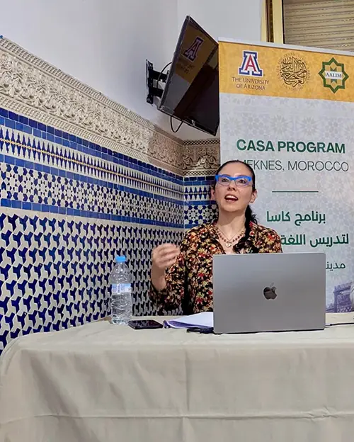 A woman speaker talking from behind a table with a laptop