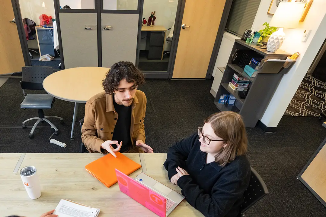 In the Herbert Writing Center, a student tutors another students on their laptop. 