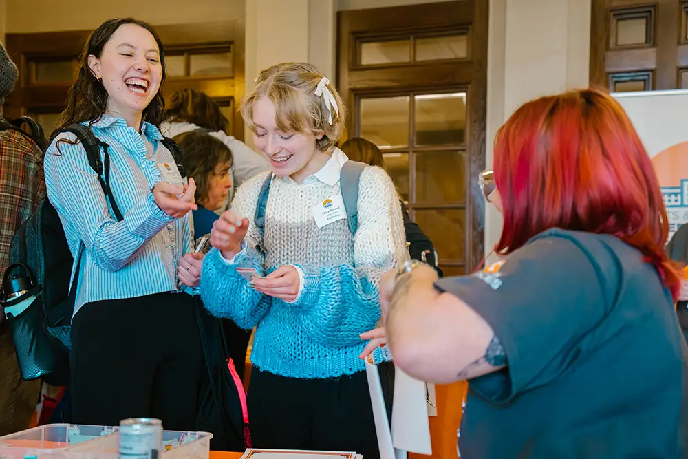 Two students laugh in line at the ASUReS event registration table.