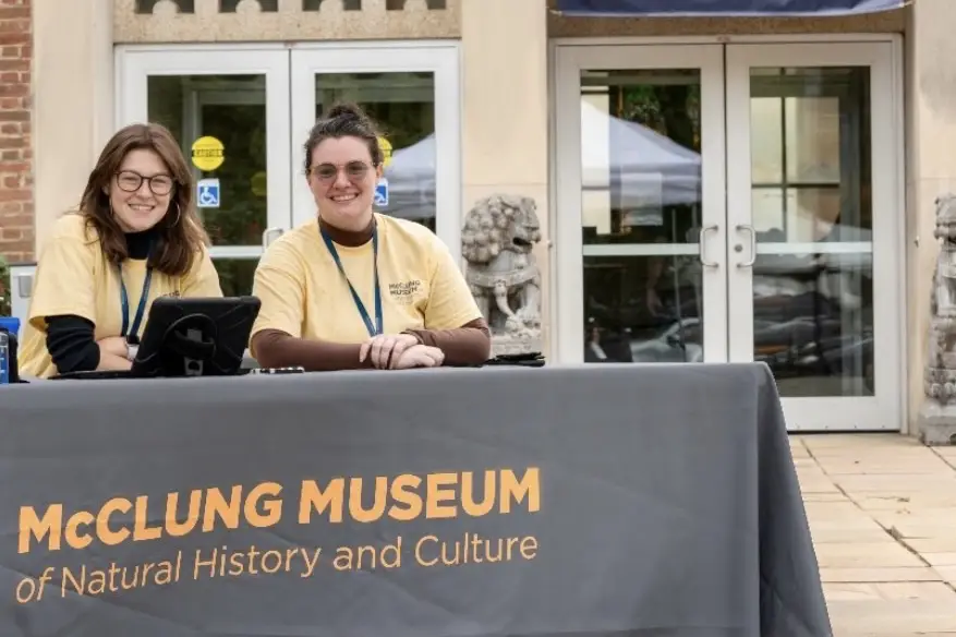 Emma Miller and Amanda Beasley sit a table outside of the McClung Museum of Natural History and Culture on the University of Tennessee, Knoxville's campus.