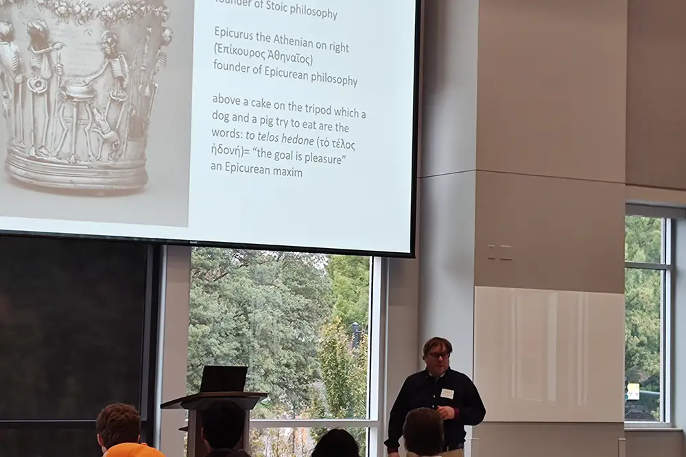 Teaching Associate Professor Dylan Bloy leads students in a lecture, standing in front of a projector. 