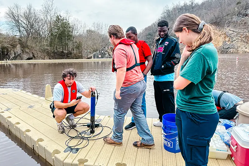Graduate students stand on the dock of Knoxville’s Mead’s Quarry Lake in spring 2024 as they collect water samples. 