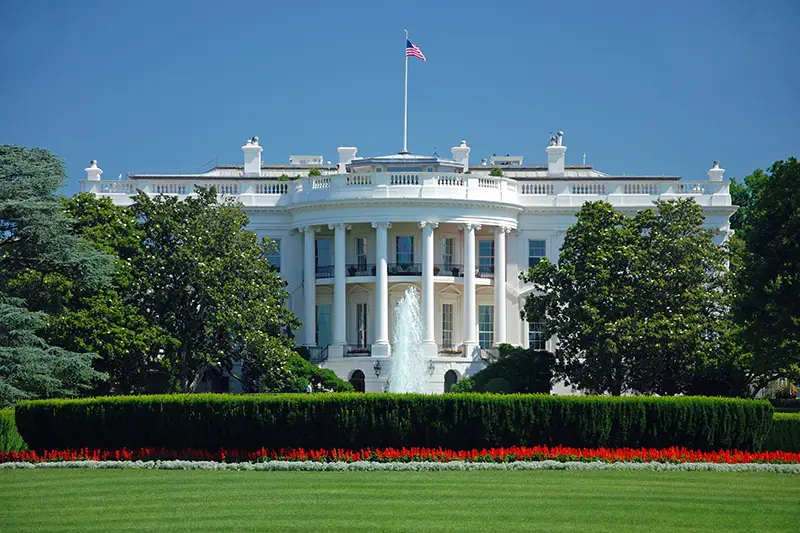 The White House in Washington, D.C. against a green lawn, blue sky, and red flowers. Image by Vacclav.