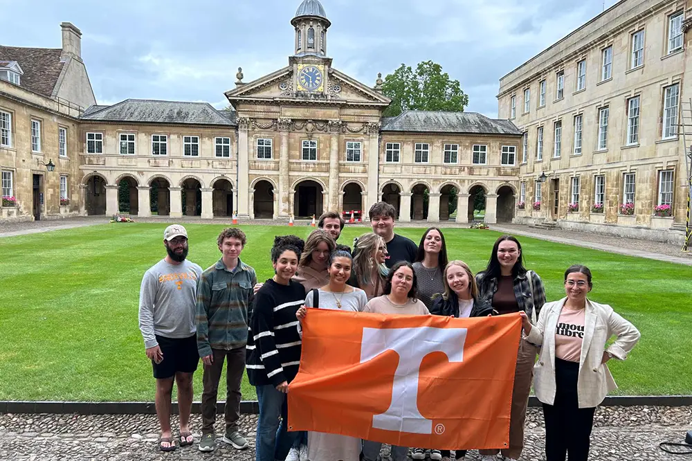 Medieval and Renaissance Studies students hold an orange power "T" flag in front of a building.