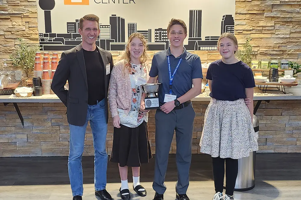 Three high school students from the Doeskin Valley Academy stand with their coach holding a runner-up trophy from the 2026 High School Ethics Bowl.