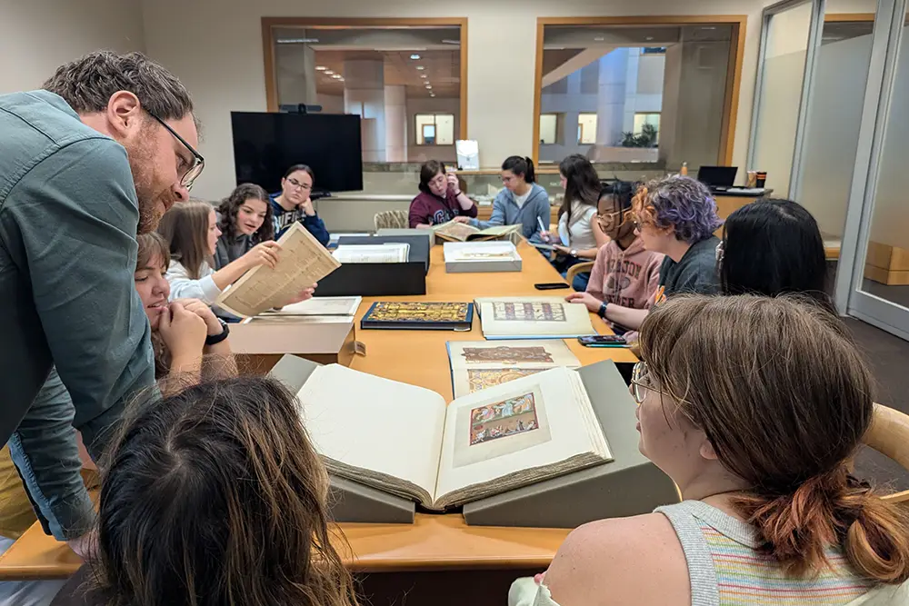 A professor stands with Medieval and Renaissance Studies students as they explore books and manuscripts from the Special Collections in Hodges Library.