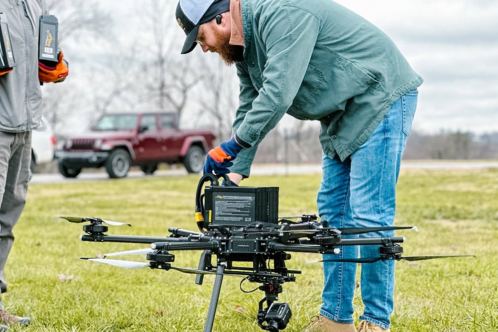 GIS Lab Manager Tim Kane prepares a UAV for launch while standing outside in a grassy field. 