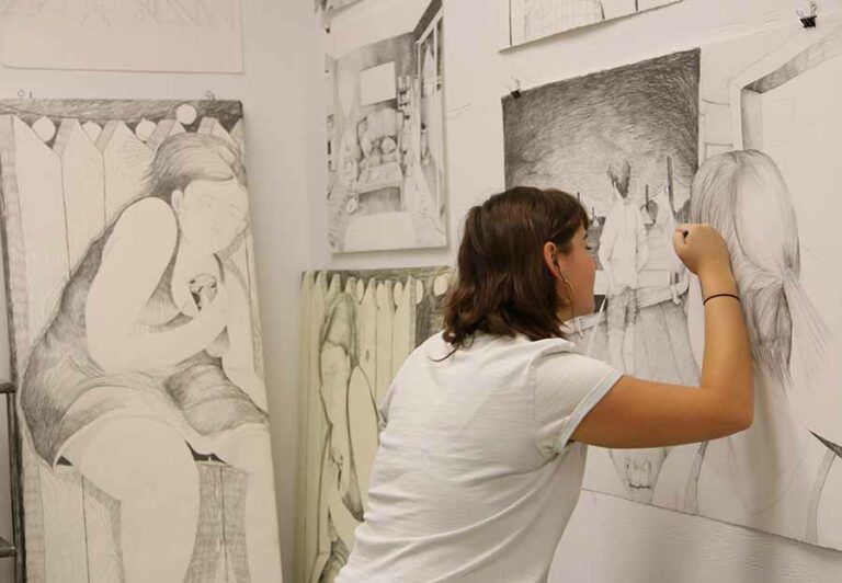 An art student works on sketches on a wall. 