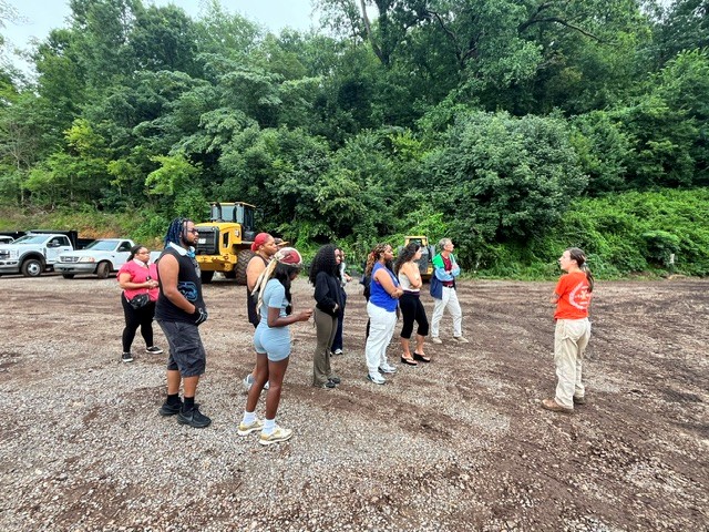 Students stand outside while a professor speaks to them on an environmental site. 